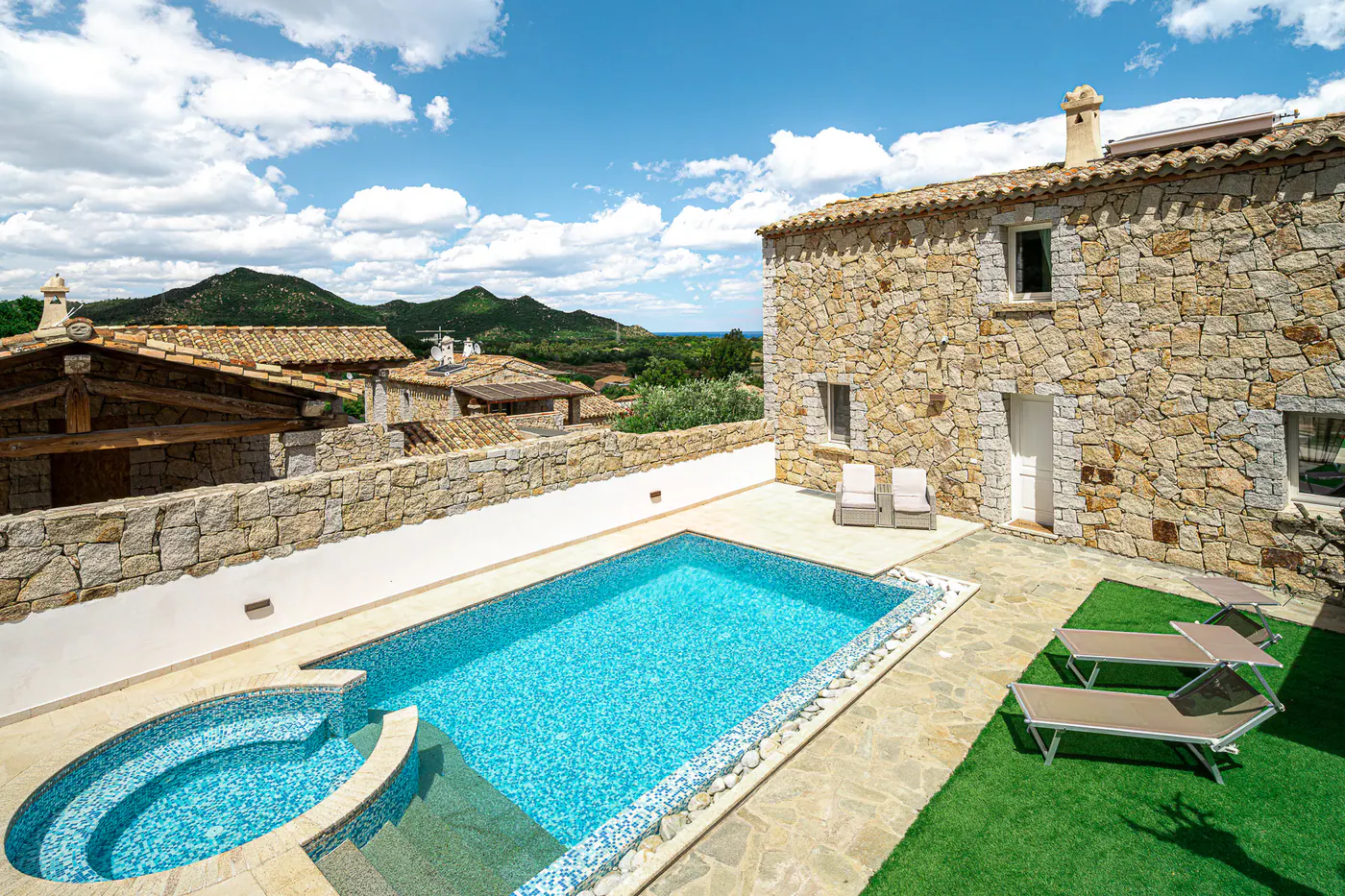 The pool with the hot tub next to the stone facade, with sun loungers on the lawn